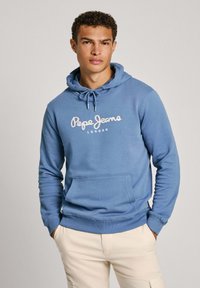 Sudadera de algodón azul con bolsillo frontal, capucha con cordón y logotipo de "Pepe Jeans London" en texto cursivo blanco. Acabado de tejido texturizado.