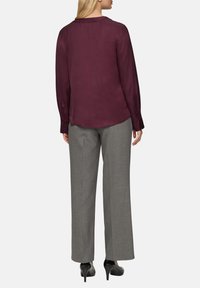 Bordeauxfarbene Bluse mit langen Ärmeln und rundem Ausschnitt, aus glattem Stoff gefertigt. Kombiniert mit grauen weit geschnittenen Hosen und schwarzen High Heels.