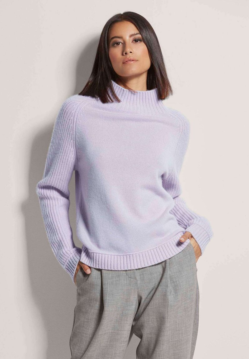 Helllila Rollkragenpullover mit gerippten Akzenten an den Ärmeln und dem Saum, kombiniert mit lockeren grauen Trousers. Weicher, strukturierter Stoff.