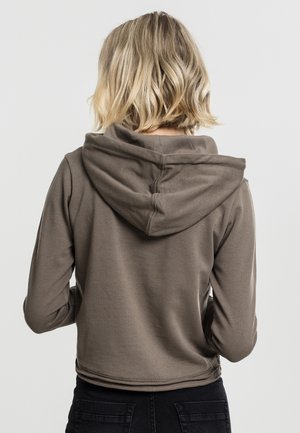 Brun cropped hoodie med en myk tekstur, med en stor hette og sømdetaljer. Bærer svarte jeans, viser bakvinkel.