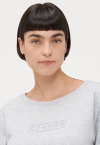 Grå hettegenser med rund hals, med en brodert "CPNHGN"-logo i en subtil nyanse på forsiden. Myk tekstur.