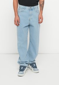 Lyseblå baggy jeans laget av denim, med høy midje, fem lommer og en falmet finish, kombinert med hvite og blå sneakers.