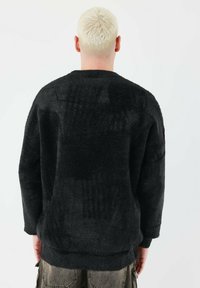 Schwarzer Fleece-Pullover mit strukturierter Oberfläche, langen Ärmeln und gerippten Bündchen. Das Design hat eine entspannte Passform mit einem Rundhalsausschnitt.