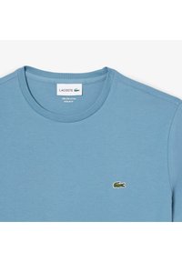 Svjetloplava majica s kratkim rukavima izrađena od 100% Pima pamuka, s okruglim izrezom i malim Lacoste krokodilom logotipom na lijevoj strani prsnog koša. Standardni kroj.