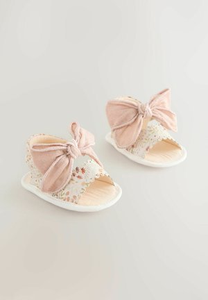 Világos rózsaszín szandálok nagy masni díszítéssel, virágmintás pántokkal, hullámos szegélyekkel és texturált bézs talppal.