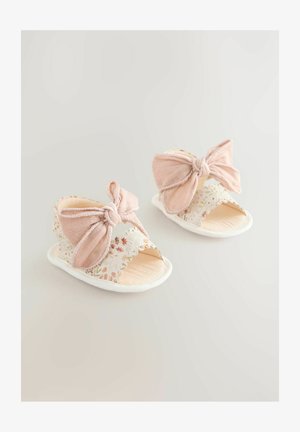 Lyserøde sandaler med store sløjfedetaljer, blomsterprintet stropper, bølgede kanter og en tekstureret beige sål.