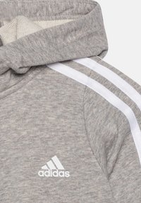 Szara bluza z kapturem o miękkiej fakturze, z białym wzorem trzech pasków na ramionach oraz wyszywanym białym logo adidas.