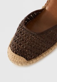 Καφέ υφαντό παπούτσι εσπαντρίγια με πλεγμένη σόλα από τζούτ και στρογγυλεμένη μύτη, που δείχνει λεπτομερή υφή και ραφές σε λευκό φόντο.