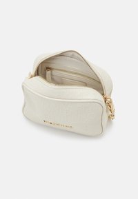 Vit präglad lädercrossbody-väska med gyllene detaljer och dragkedjestängning. Inuti finns två fack och en släppficka för bättre organisering.