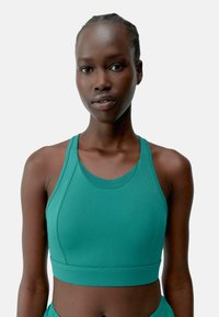 Reggiseno sportivo verde acqua realizzato in tessuto elasticizzato, con design a schiena scoperta, ampia fascia sotto il busto e superficie liscia con cuciture piatte per il massimo comfort.