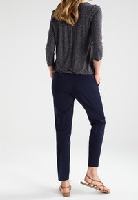 Mörkblå byxor med skräddarsydd passform och slät textur, kombinerade med en mörk mönstrad blus med trekvartslånga ärmar och rundad halsringning.