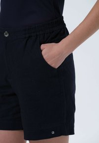 Marineblaue Shorts aus leichtem Stoff, mit elastischem Bund, Seitentaschen und einem kleinen Logoakzent nahe dem Saum.