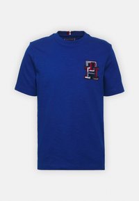 Modré bavlněné tričko s kulatým výstřihem a krátkými rukávy. Na levé straně hrudi je vícebarevné vyšívané logo. Hladká textura.