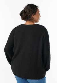 Črn, teksturiran pulover z rahlo oprijetim krojem in širokimi rokavi ter okroglim izrezom. Nošen z modrimi kavbojkami iz jeansa.