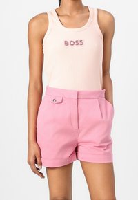 Světle růžový top na ramínka s nápisem "BOSS" z kamínků, v kombinaci s růžovými šortkami s vysokým pasem, plochým předním dílem a zabořenými manžetami.