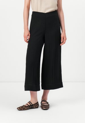 Black wide-leg pleated pants with a high waistband, featuring a textured fabric. Styled with leopard print flats with two straps.