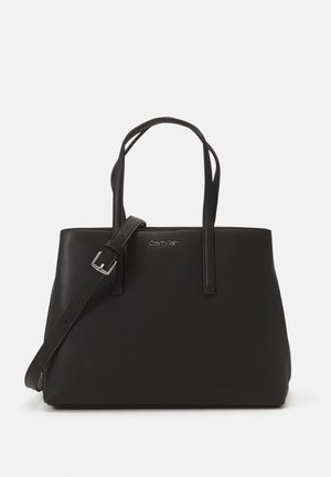 Czarna torba typu tote Calvin Klein z dwoma paskami na ramię i jednym regulowanym paskiem do noszenia na ukos na białym tle.