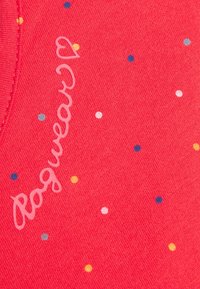 Červená bavlněná látka se skvrnami v mnoha barvách a slovy "Rogwear" v světle růžovém kurzívním písmu.