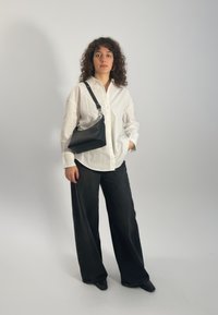 Melnas ādas plecu soma ar izliekta formas, sudraba aparatūru un regulējamu siksnu. Nēsāta ar baltu pogājamu kreklu un melnas platu kāju džinsām.