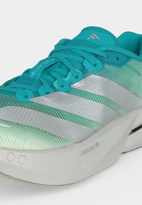 Chaussure de running légère turquoise avec des bandes argentées, semelle blanche amortissante étiquetée « LIGHTSTRIKE PRO » et « FOLLOW THE LINE » imprimé sur la languette.
