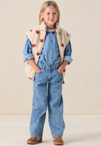 Veste en denim et jeans avec motifs de cœurs rouges, gilet en polaire crème avec taches rouges, chaussures marron, couleurs unies, coupe décontractée, style relaxed.