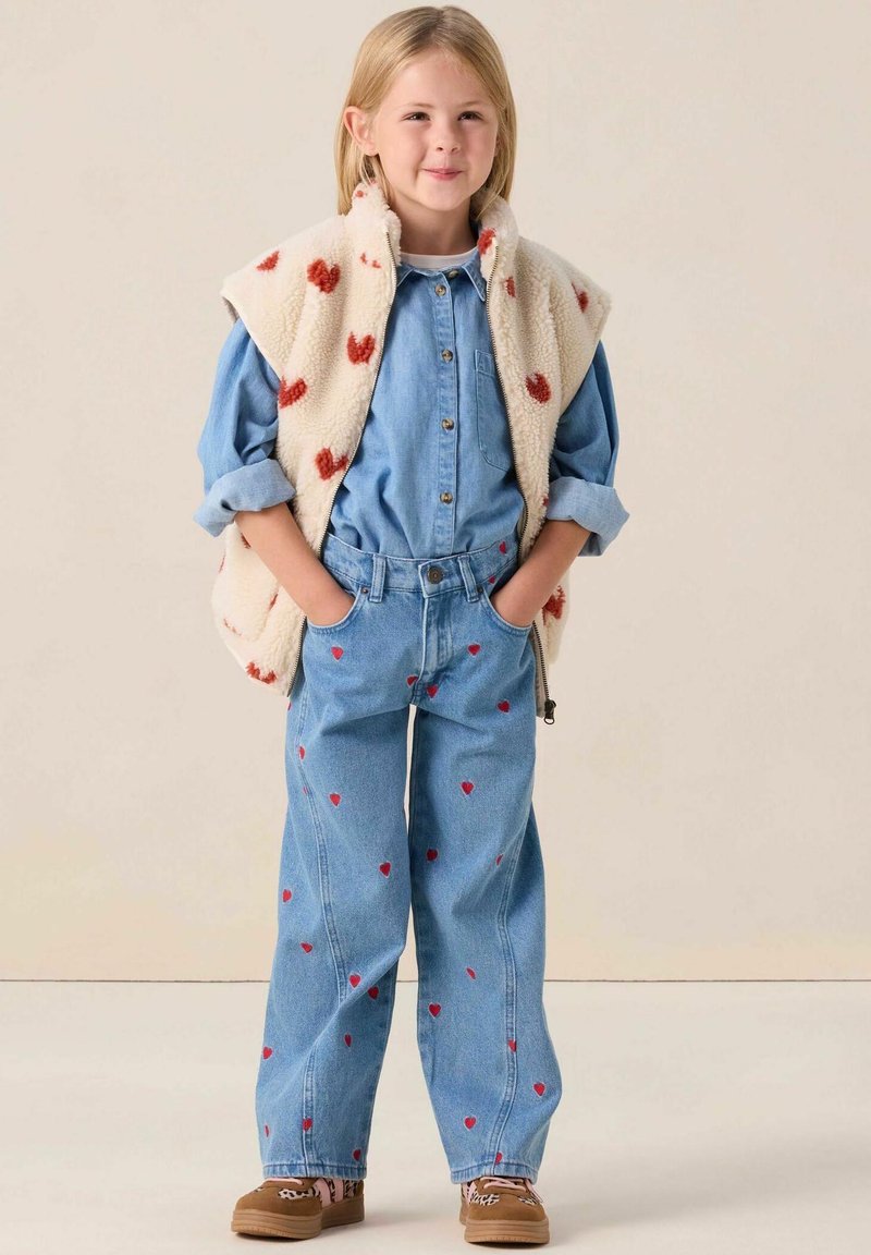 Veste en denim et jeans avec motifs de cœurs rouges, gilet en polaire crème avec taches rouges, chaussures marron, couleurs unies, coupe décontractée, style relaxed.