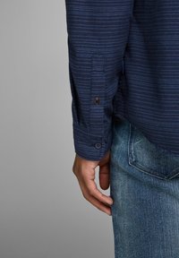 Mörkblå randig långärmad skjorta med knappade manschetter, kombinerad med ljusblå jeans. Har en slät textur och subtila detaljer.