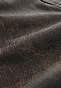 Tejido texturizado en marrón oscuro con un patrón arrugado y un brillo sutil, mostrando un primer plano de la superficie del material.