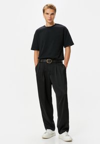 Mustat lyhythihaiset t-paidat yhdistettynä korkeavyötäröisiin mustiin housuihin, joissa on poimutuksia, musta vyö pyöreällä soljella ja valkoiset lenkkarit.