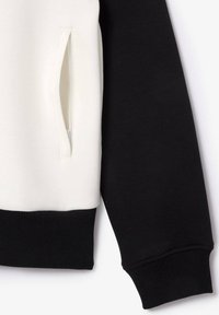 Manche de sweat-shirt noir et blanc avec une poche zippée sur la section blanche et des poignets côtelés noirs en bas.