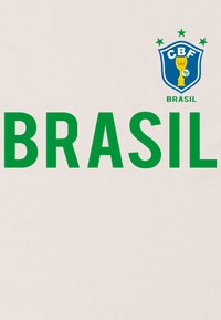 Koszulka na jasnym kremowym tle z dużym zielonym napisem "BRASIL" oraz niebieskim emblematem z gwiazdami i trofeum powyżej.