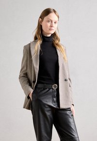 Blazer în carouri maro, cu două rânduri de nasturi, combinat cu un pulover cu gât negru și pantaloni din piele negri. Prezintă o talie curea.