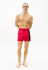 Shorts de bain rouges avec une taille élastique à cordon, présentant un panneau latéral noir et blanc. Tissu léger, design au-dessus du genou.