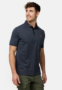 Marineblå polo t-shirt med tekstureret finish, korte ærmer og en kontrastfarvet sort krave. Har tre knapper og et orange logo på brystet.
