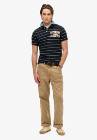 Marine gestreepte polo met een dennenhals, beige chino's en lichte sneakers. Beschikt over een logo op de borst en een zwarte riem.