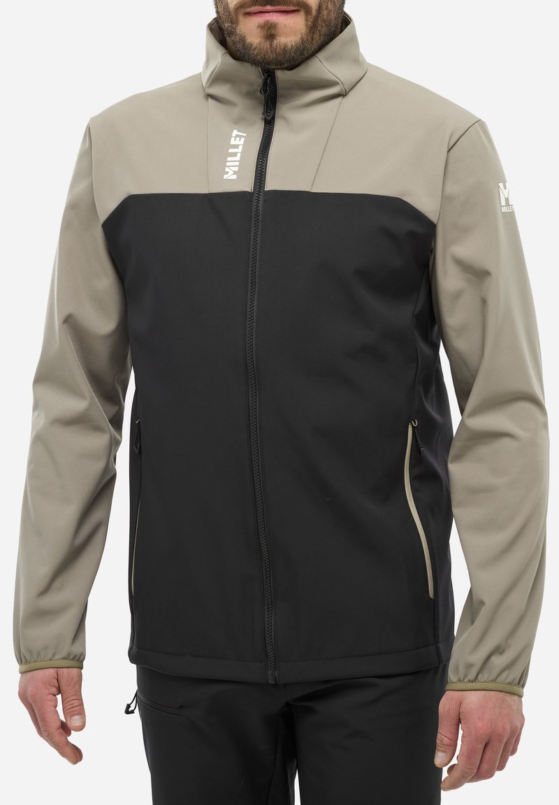 Veste softshell noire et beige avec un col haut, des poches latérales et une fermeture éclair. Tissu texturé avec des blocs de couleur contrastés.