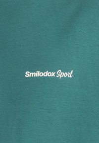 Camiseta de algodón en color verde azulado con el texto blanco "Smilodox Sport" en el centro. Textura suave con un diseño clásico de cuello redondo.