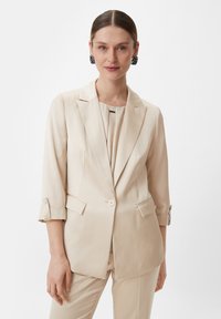 Beige blazer with a tailored design, notch lapels, two pockets, single button closure, and rolled-up sleeves. Smooth, lightweight fabric.