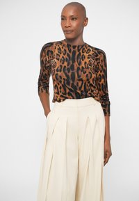 Leopardmönstrad tröja i bruna och svarta nyanser med lång ärm, parat med högmidjade krämfärgade byxor med veck. Enkla former.