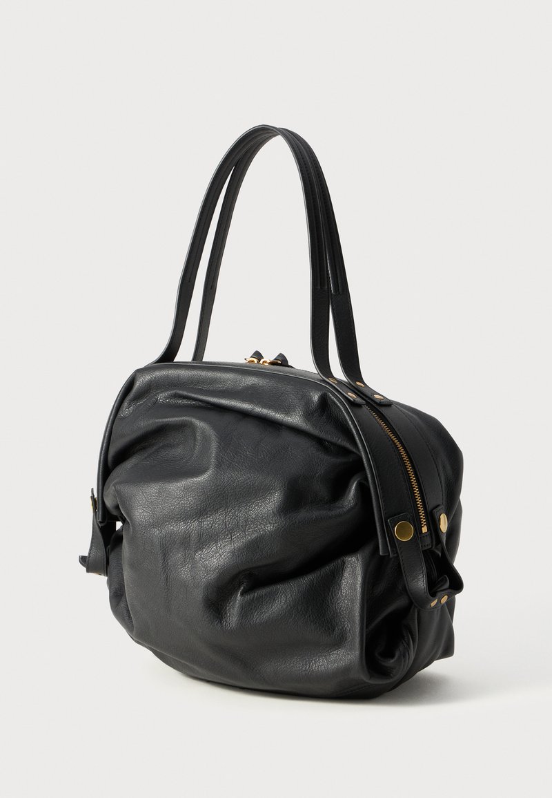 Sac en cuir noir avec une finition texturée. Dispose d'une forme arrondie, de deux poignées supérieures et d'une fermeture éclair dorée. Les accents comprennent du matériel en laiton.