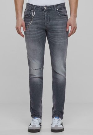Jeans de mezclilla gris con un corte ajustado, que presentan un roto en la rodilla, un ligero desgaste y un detalle de cadena de metal en el bolsillo.