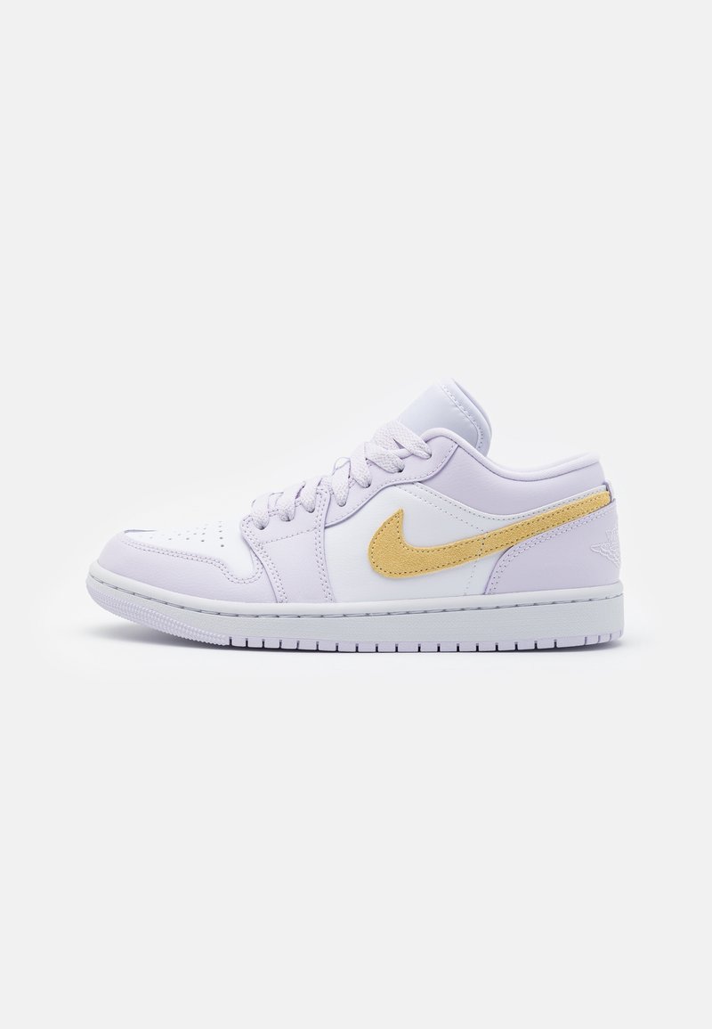 Baskets basses blanches avec le logo Nike jaune, lacets blancs et bout perforé sur un fond clair uni.