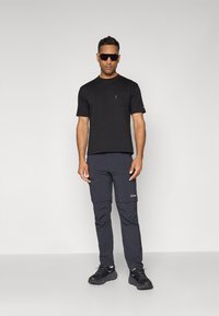 Black short-sleeve t-shirt with a front pocket, paired with navy cargo pants featuring zippered pockets and reinforced stitching. Black sneakers.