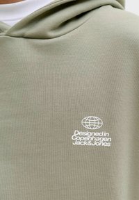 Svetlozelená mikina s kapucňou a bielym textom a logom zemegule s nápisom "Navrhnuté v Kodani Jack & Jones" na oblasti hrude.