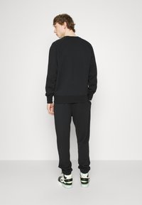 Must must ja sobivad dressipüksid, millel on ribadega varrukad ja alläär. Kandmine mustade ja valgete tennistega. Üksikasjalik taust.