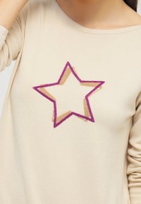 Beige Langarmshirt mit einem mehrfarbigen Sternen design, das von rosa und beige umrandet ist, aus weichem, leichtem Stoff.