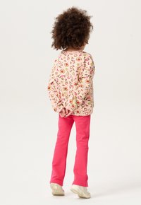 Roze sweatshirt met bloemenpatroon en lange mouwen, gecombineerd met felroze broek en lichtgekleurde sneakers. Zicht van achteren.