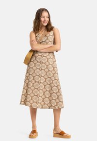 Brun mönstrad klänning med vita blommönster, ärmlös, A-linjeformad. Matchad med bruna plattformssandaler och en brun axelväska.