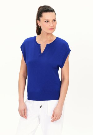 Suéter de punto de manga corta azul con cuello en V y dobladillo acanalado. Textura suave con un ajuste relajado, combinado con pantalones blancos.