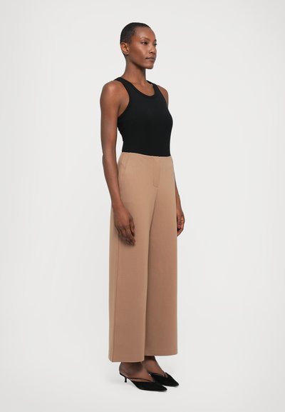 Svart ribbet tank topp kombinert med lysebrune vide bukser. Modellen har på seg svarte spisse hæler. Glatt stoff med minimal detaljering.